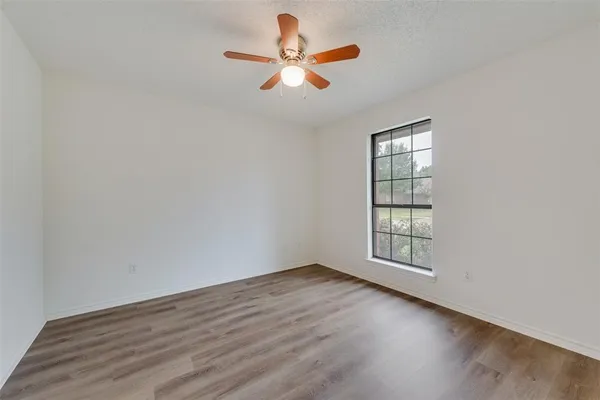 an empty room with wooden floor chandelier fan and windows
