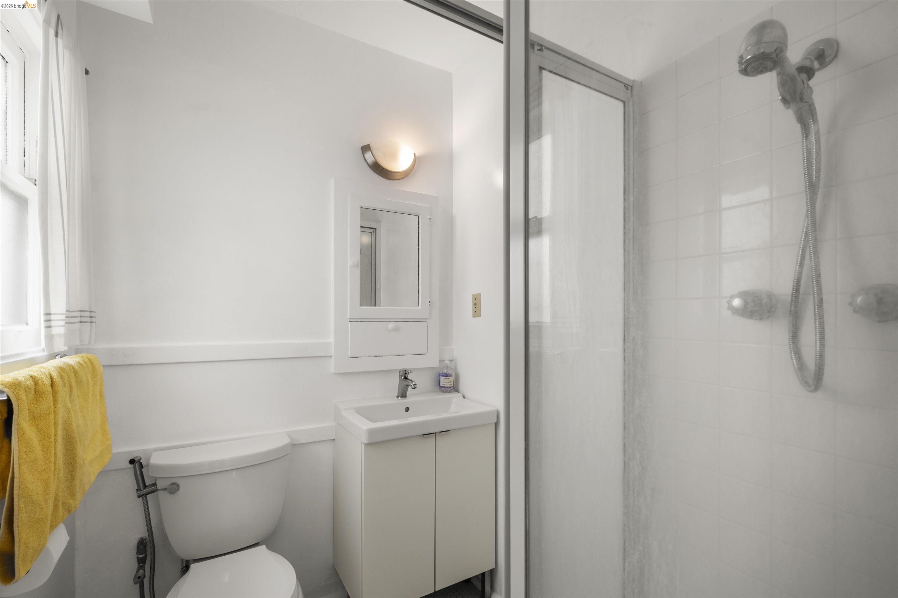 2444 Virginia Street, Unit B Berkeley, CA 94709 - Photo 34 of 39 Bathroom featuring a white vanity with a rectangular sink, wall-mounted light fixture, mirrored medicine cabinet, and a glass-enclosed shower with a handheld showerhead