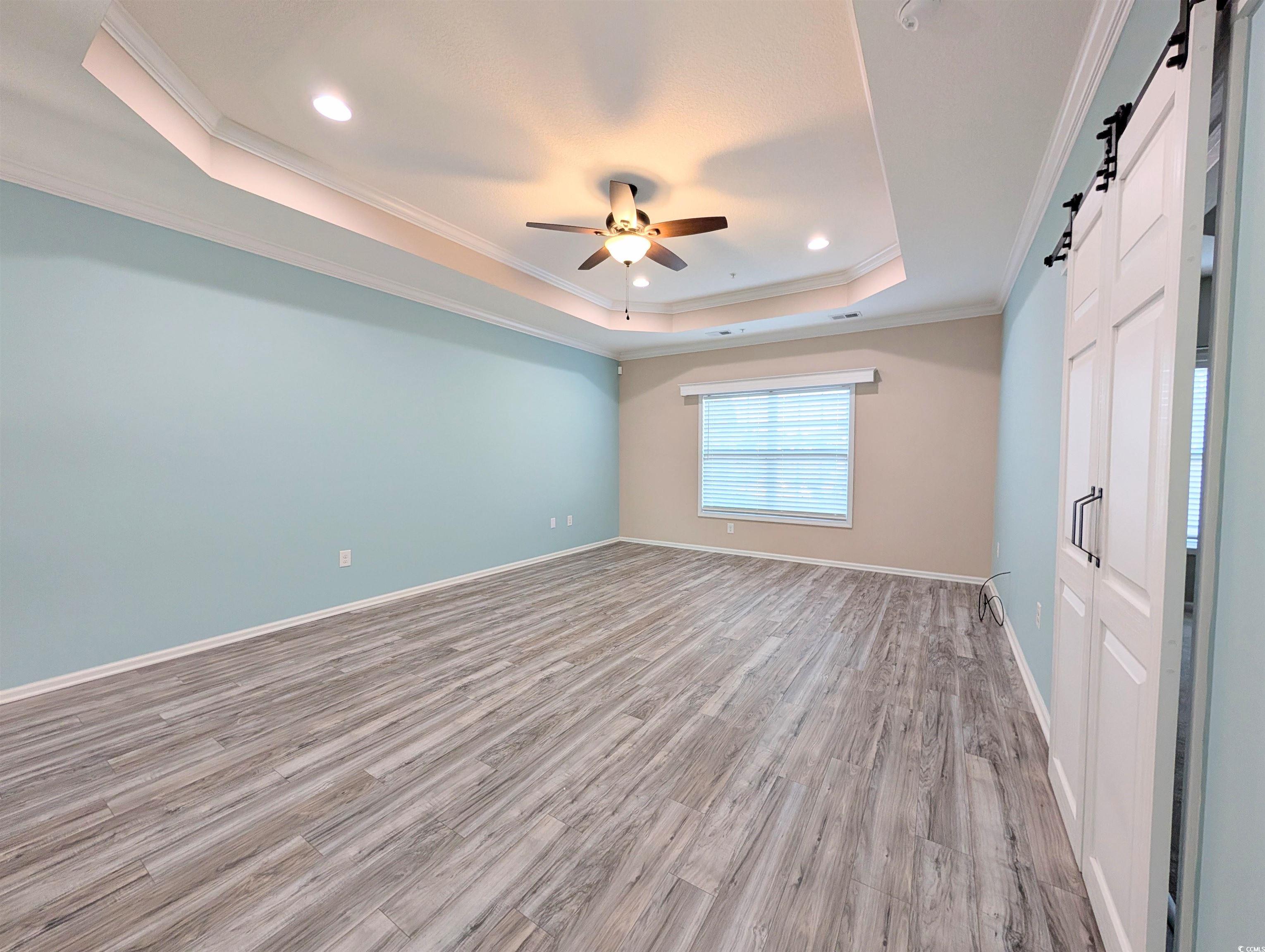 822 Sail Lane Murrells Inlet, SC 29576 - Photo 14 of 34 Unfurnished room featuring a barn door, ornamental molding, a tray ceiling, wood finished floors, and ceiling fan