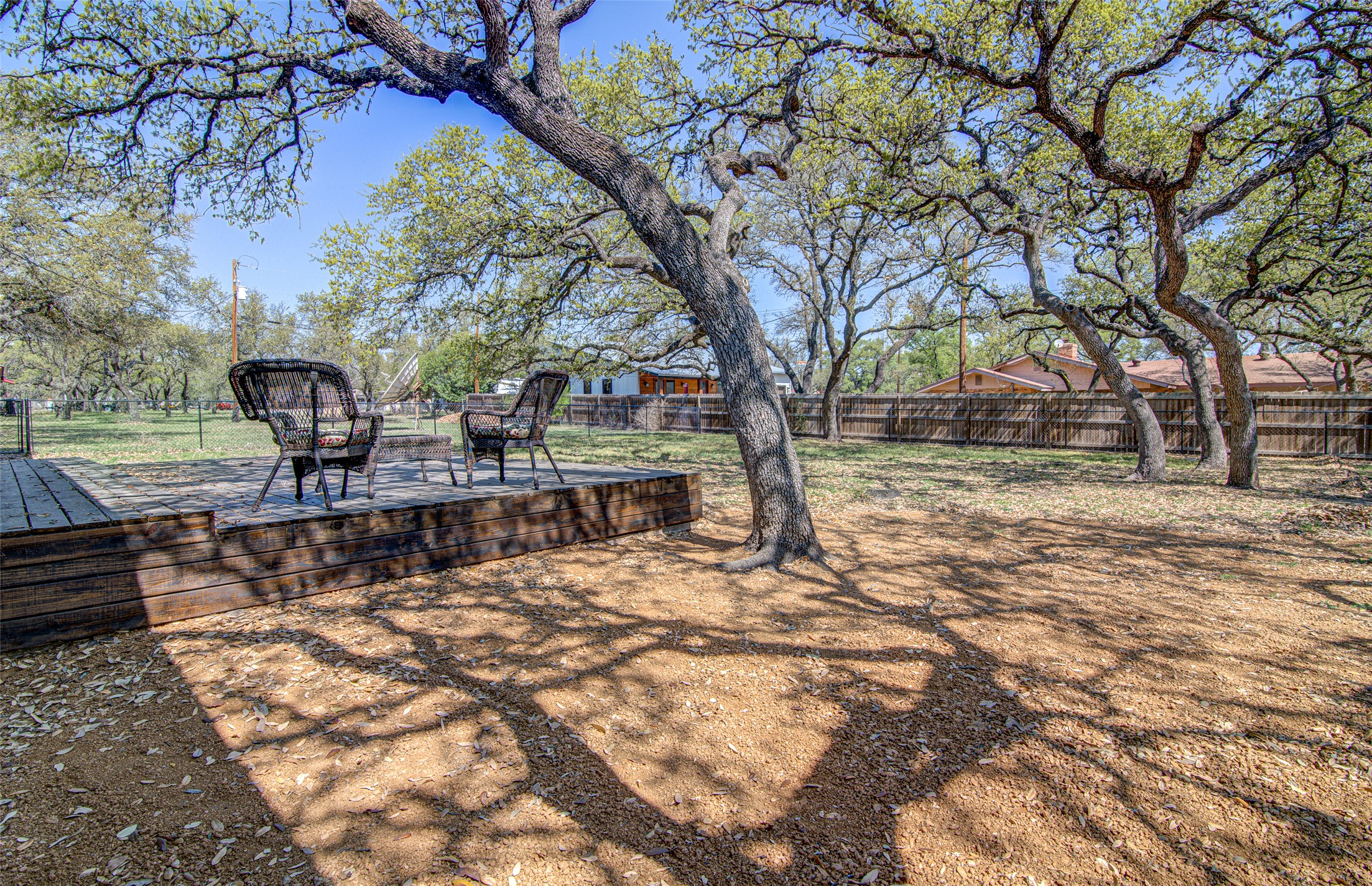 207 Haley Road Johnson City, TX 78636 - Photo 29 of 31 A spacious backyard with mature trees providing shade over a raised wooden deck, perfect for outdoor relaxation.