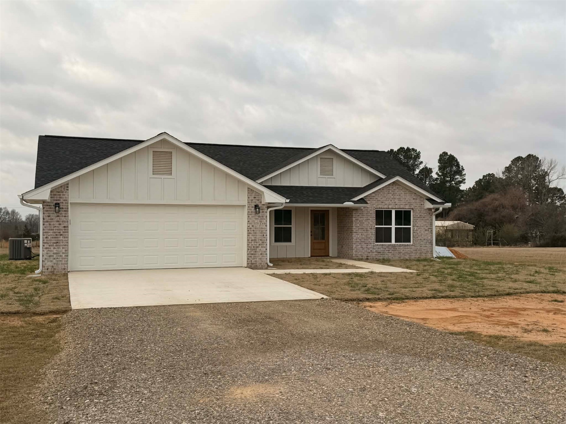 2911 East 2090 Road Hugo, OK 74743 - Photo 1 of 22 Brick and vertical siding exterior with a dark shingle roof, attached two-car garage, and a light wood-finish front door