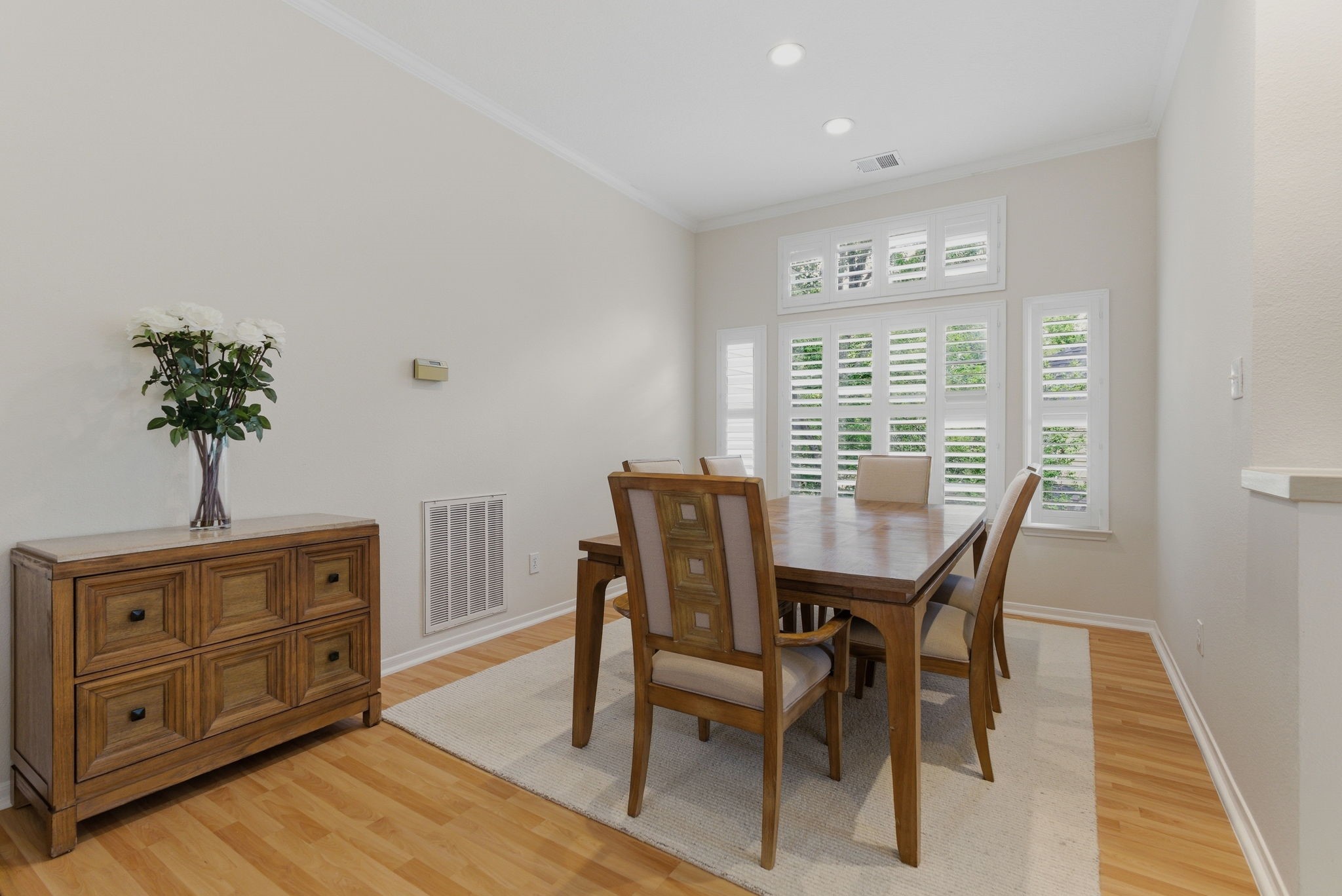 11 Dovewing Place Spring, TX 77382 - Photo 8 of 32 This dining room features a warm, inviting space with light wood flooring, a wooden dining table with six chairs, and large windows with plantation shutters for natural light. The neutral walls and simple decor create a cozy and elegant atmosphere.