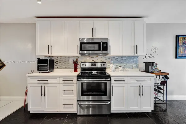a kitchen with stainless steel appliances kitchen island granite countertop a stove top oven a sink a dining table and chairs with white cabinets