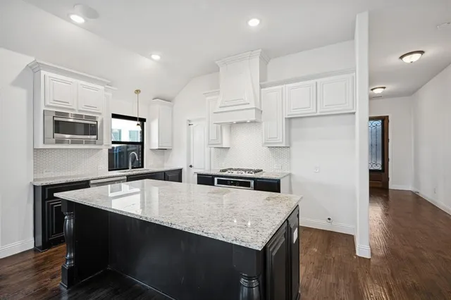 a kitchen with stainless steel appliances granite countertop a sink dishwasher a refrigerator a stove a microwave oven with white cabinets and wooden floor