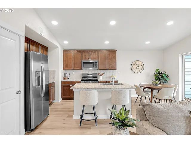 a kitchen with stainless steel appliances granite countertop a refrigerator a stove a sink a dining table and chairs with wooden floor