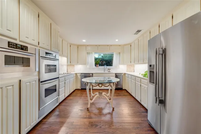a kitchen with stainless steel appliances a refrigerator a stove a sink and white cabinets