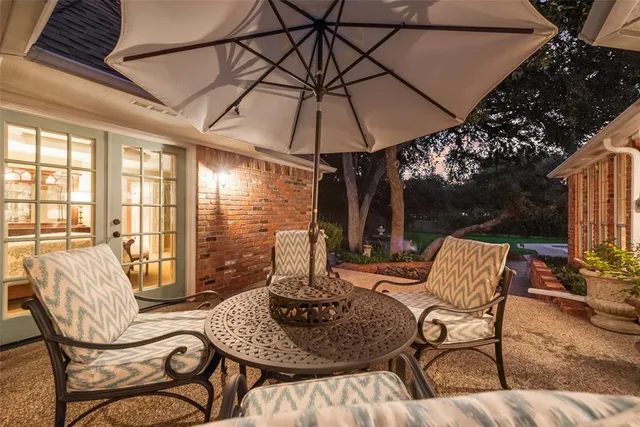 a view of a patio with a dining table and chairs under an umbrella with a small yard