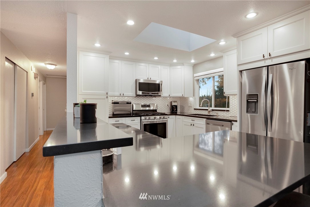 10727 126th Avenue Northeast Kirkland, WA 98033 - Photo 10 of 40 a kitchen with stainless steel appliances a refrigerator a stove a sink a oven with white cabinets and wooden floor
