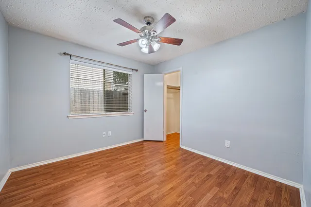 a view of an empty room with wooden floor and a ceiling fan