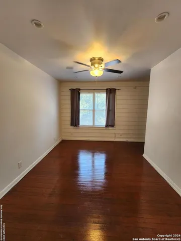 a view of empty room with wooden floor and fan