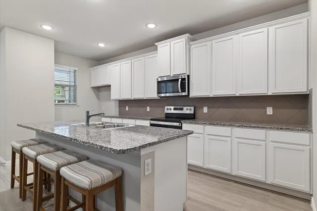 a kitchen with stainless steel appliances granite countertop a sink a stove a microwave a refrigerator and white cabinets