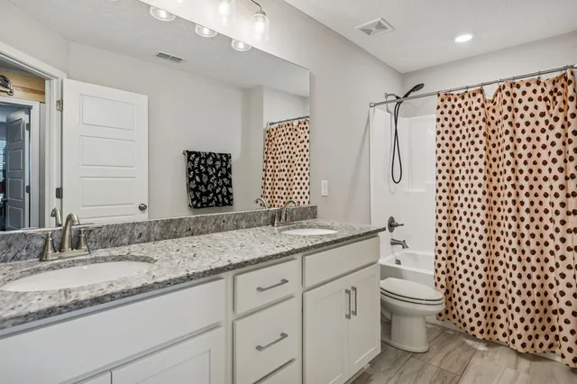 a en suite bathroom with a granite countertop double vanity sink a mirror and shower