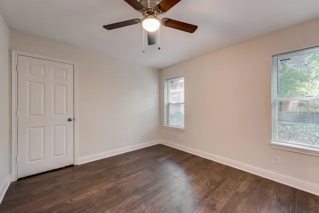 an empty room with wooden floor fan and windows
