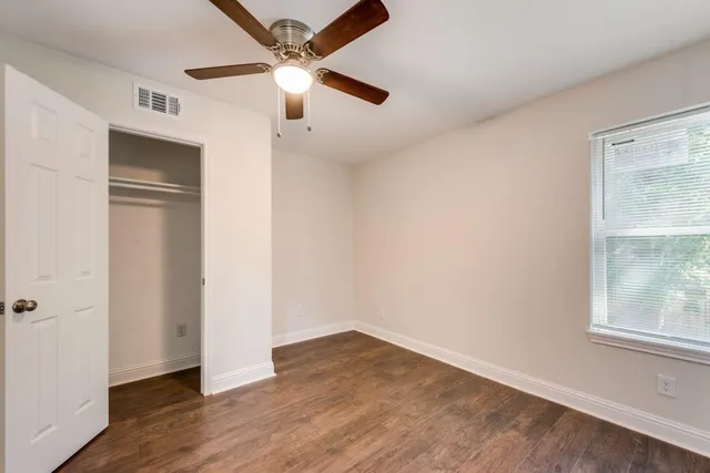 an empty room with wooden floor fan and windows