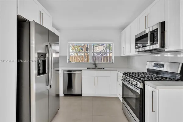 a kitchen with stainless steel appliances granite countertop white cabinets a sink a stove a microwave and a refrigerator