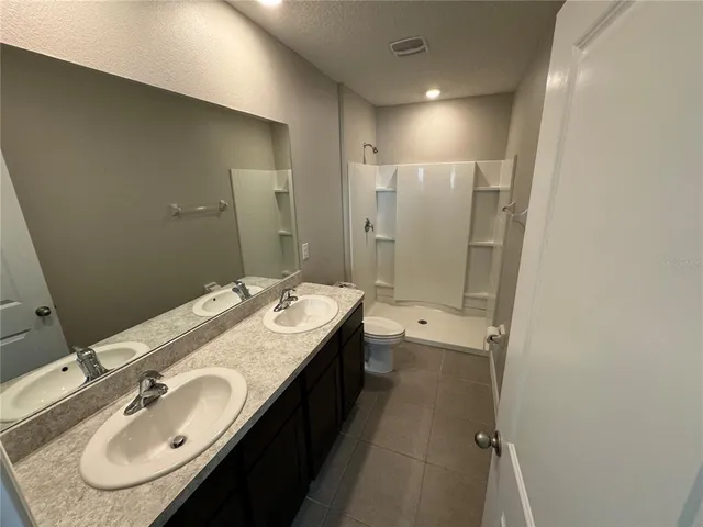 a bathroom with a granite countertop double vanity sink a mirror and a shower