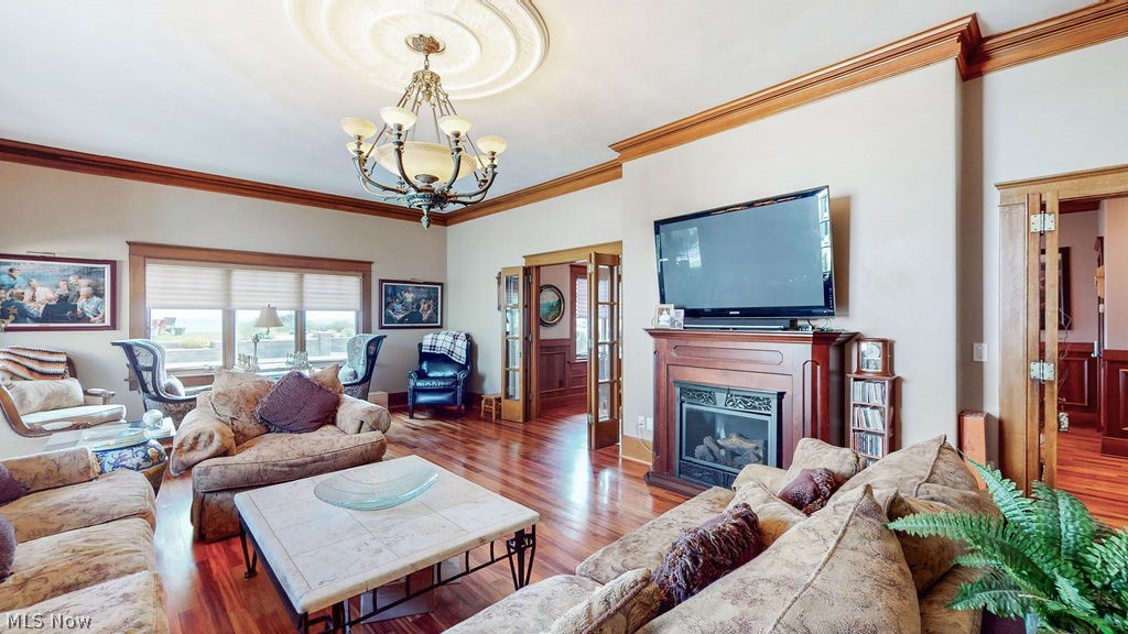 1431 Cedar Point Road Sandusky, OH 44870 - Photo 15 of 50 Living room featuring a chandelier, ornamental molding, wood finished floors, and a glass covered fireplace