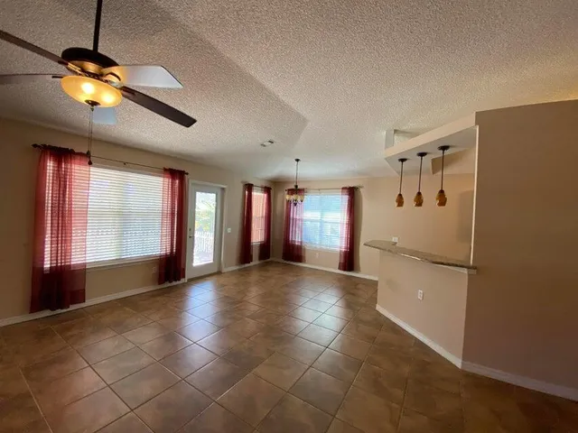 a view of an empty room with window and chandelier fan