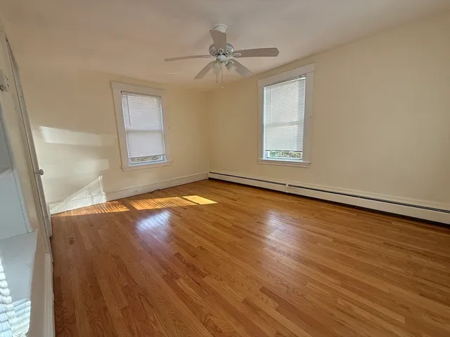 an empty room with wooden floor fan and windows