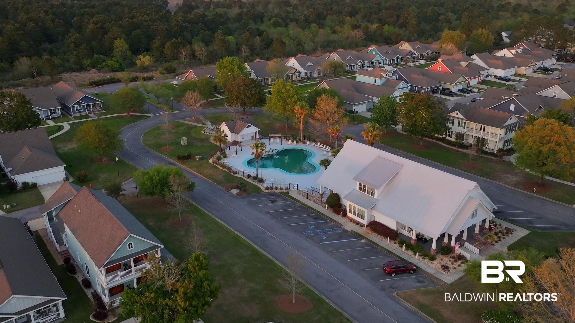 927 Periwinkle Lane Foley, AL 36535 - Photo 18 of 26 Community clubhouse with a gabled metal roof, surrounded by a swimming pool with a paved surround, ample parking, and mature landscaping