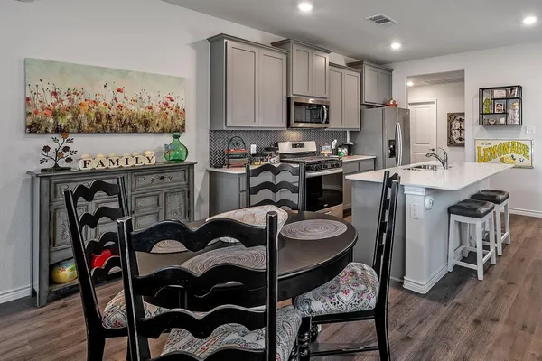a kitchen with stainless steel appliances kitchen island granite countertop a refrigerator a stove a sink dishwasher and a dining table with wooden floor