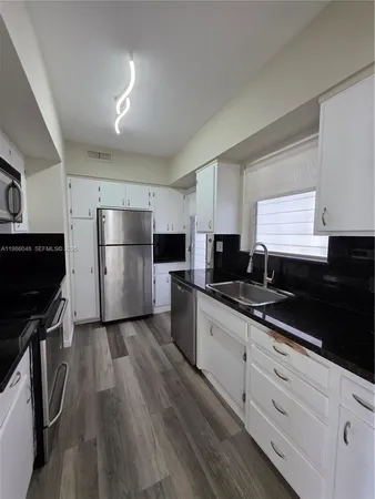 a kitchen with granite countertop a refrigerator a sink and wooden floors