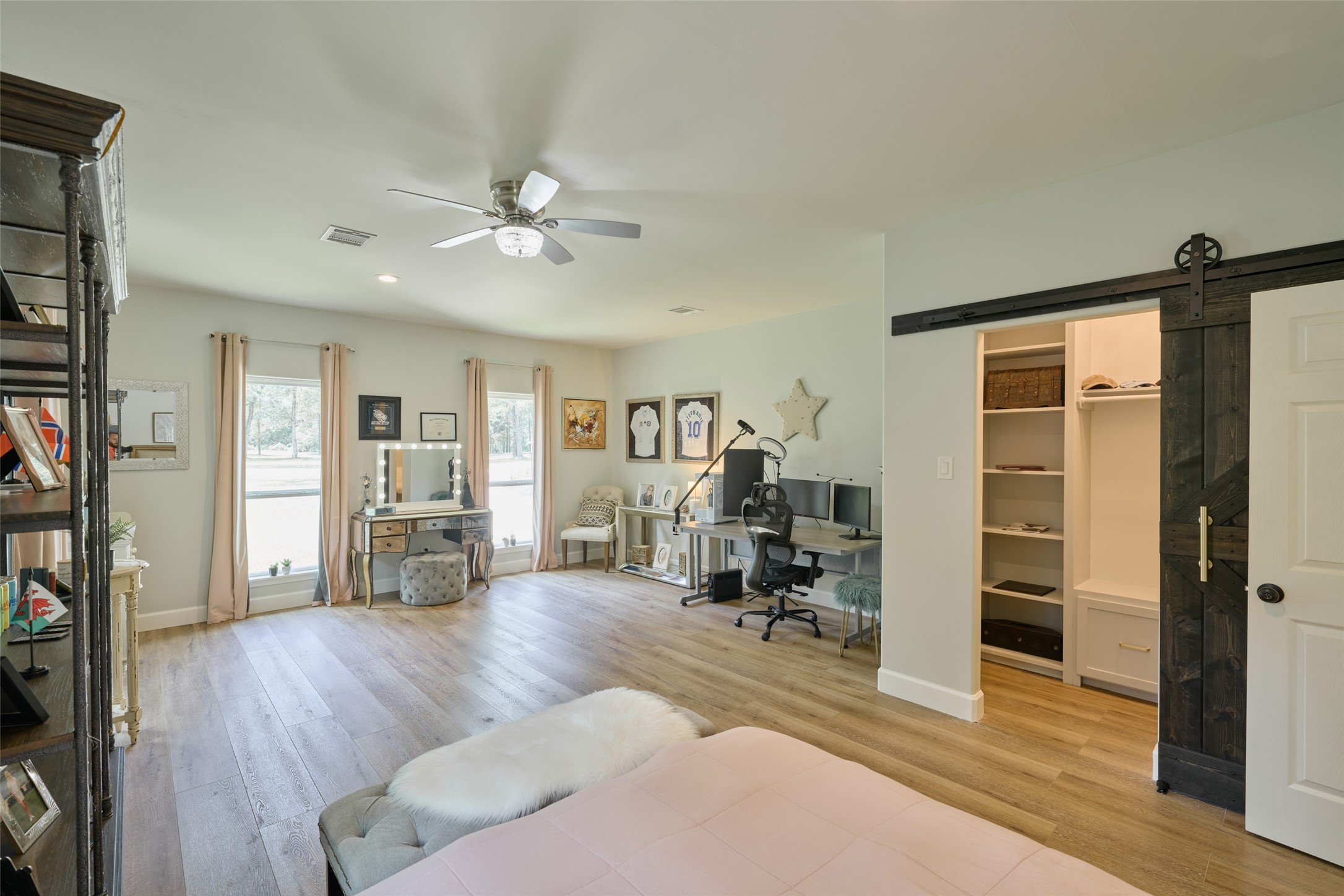 2218 Honea Egypt Road Magnolia, TX 77354 - Photo 47 of 50 This is a spacious room featuring hardwood flooring, ample natural light through large windows with elegant curtains, and a modern ceiling fan. A distinctive sliding barn door adds character and leads to a built-in closet or storage area. The room is currently furnished with a mix of office and living space decor.