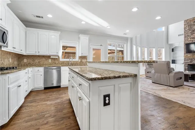 a kitchen with stainless steel appliances granite countertop a stove top oven a sink dishwasher a dining table and chairs with wooden floor