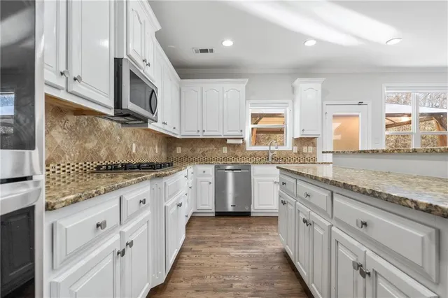 a kitchen with granite countertop white cabinets stainless steel appliances a sink and a counter top space