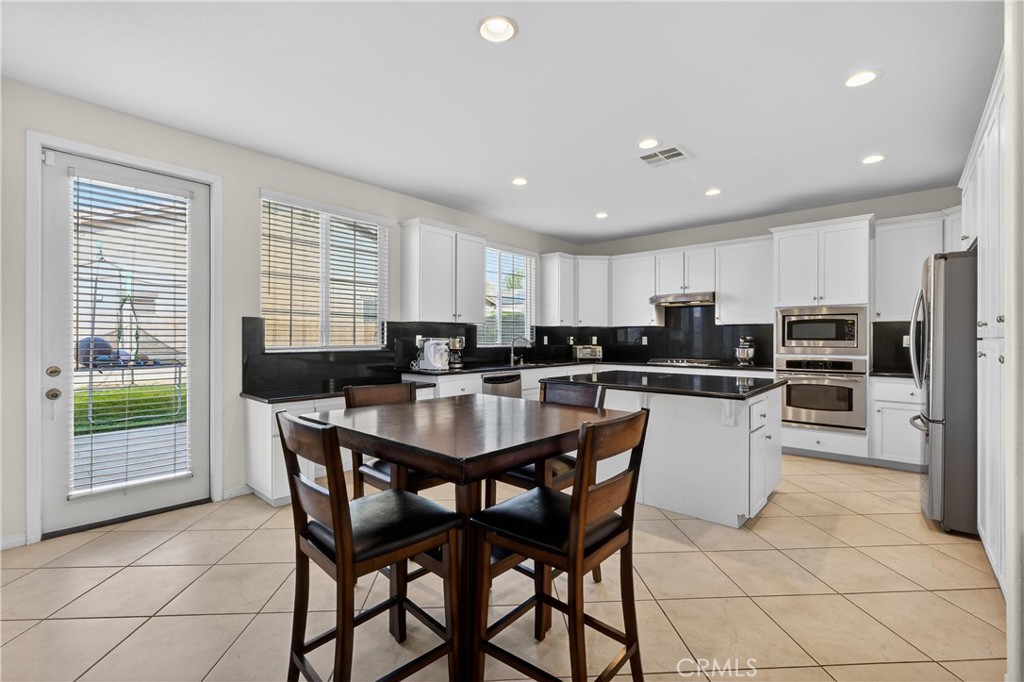 34581 Spindle Tree Street Winchester, CA 92596 - Photo 22 of 50 a kitchen with stainless steel appliances kitchen island granite countertop a refrigerator a stove a sink a dining table and chairs