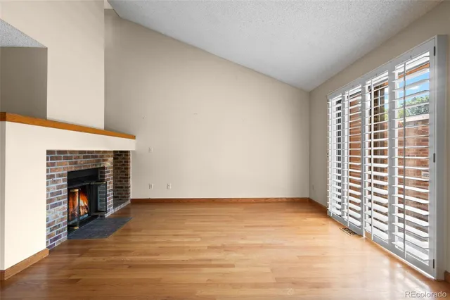 a view of an empty room with wooden floor fireplace and a window