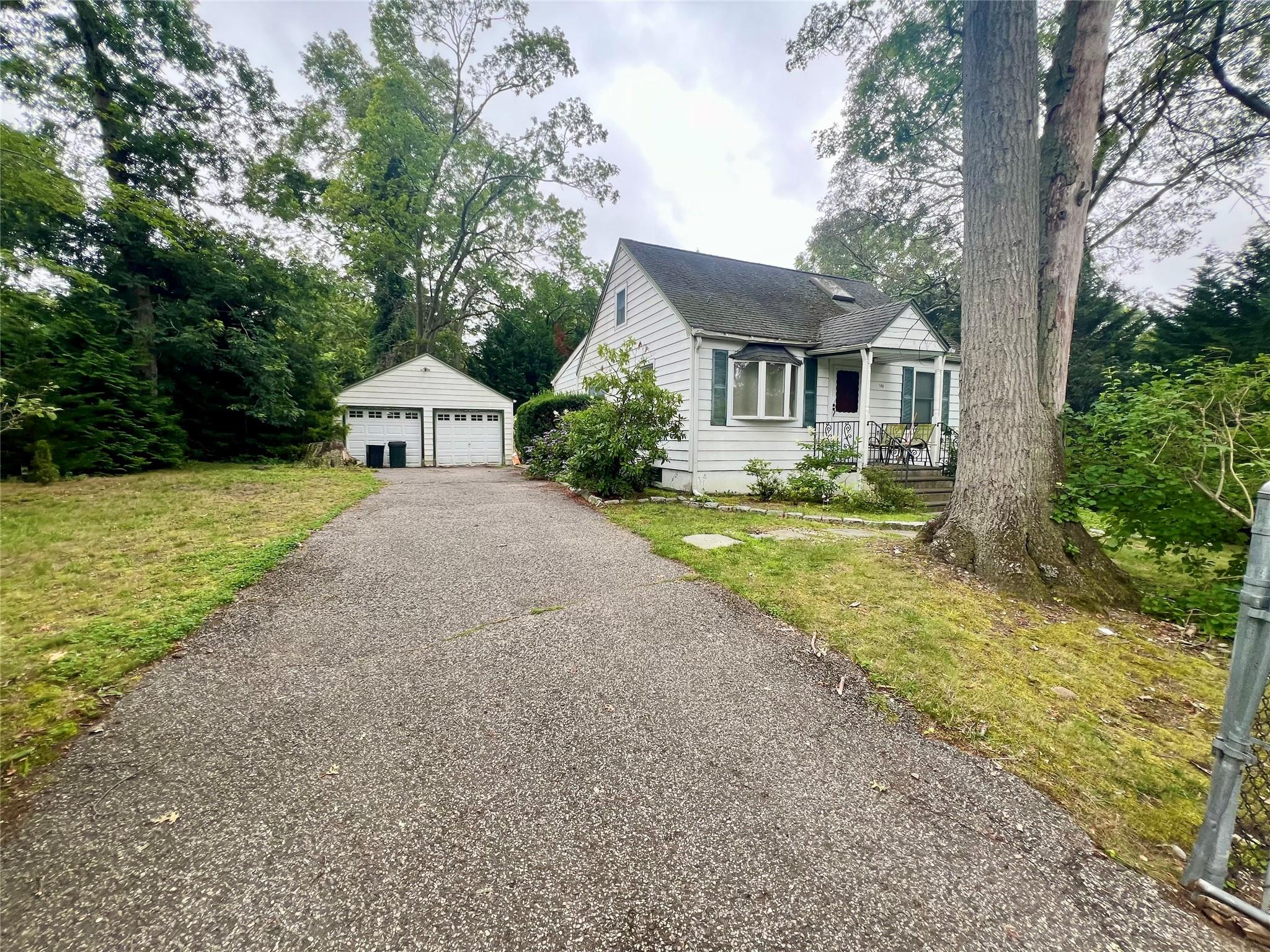 View of front of house featuring an outbuilding, a detached garage, a shingled roof, and a front yard