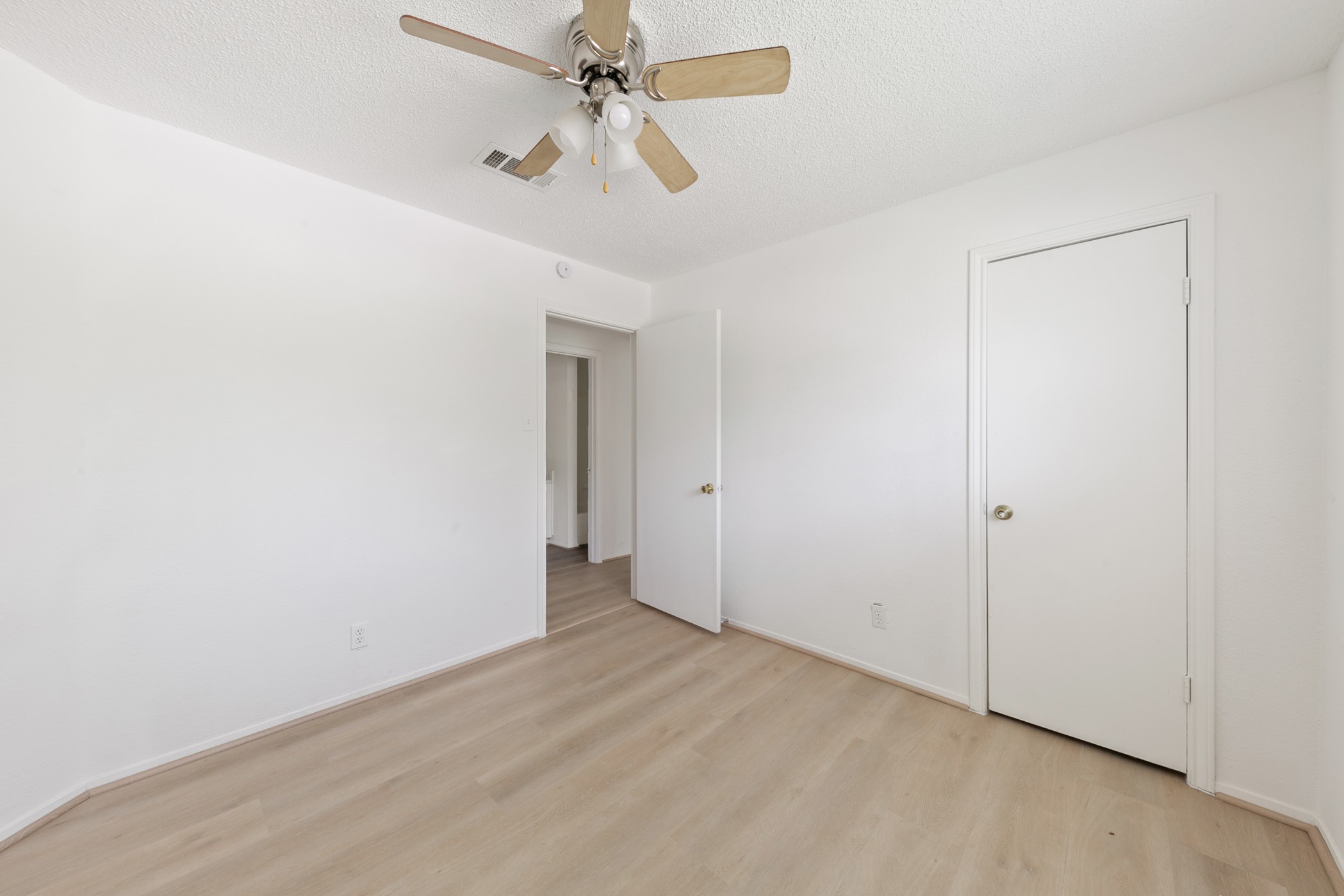 700 Lyle W Avenue, Unit D Cleveland, TX 77327 - Photo 2 of 16 This photo shows a bright, empty room with light wood flooring, white walls, a ceiling fan, and a door leading to another space. Perfect for customization.