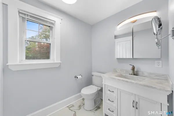 a bathroom with a granite countertop toilet a sink a mirror and a window