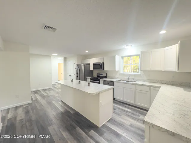 a large white kitchen with kitchen island a sink a stove a center island and furniture