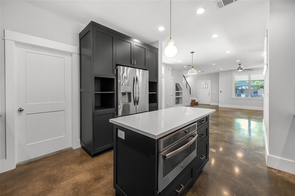 2821 Castro Street, Unit 1 Austin, TX 78702 - Photo 9 of 21 Modern kitchen featuring a dark cabinetry island with a built-in microwave, white countertop, and stainless steel refrigerator
