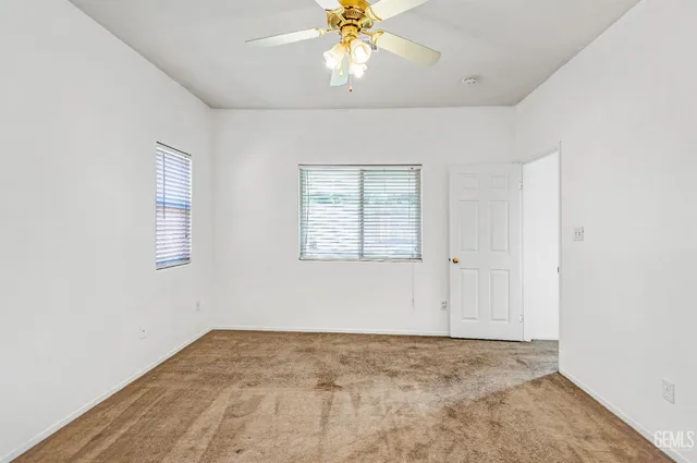 an empty room with chandelier fan and windows