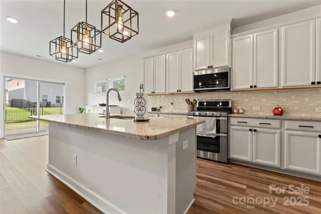 a kitchen with stainless steel appliances granite countertop a sink dishwasher a stove a microwave oven a refrigerator with white cabinets and wooden floor