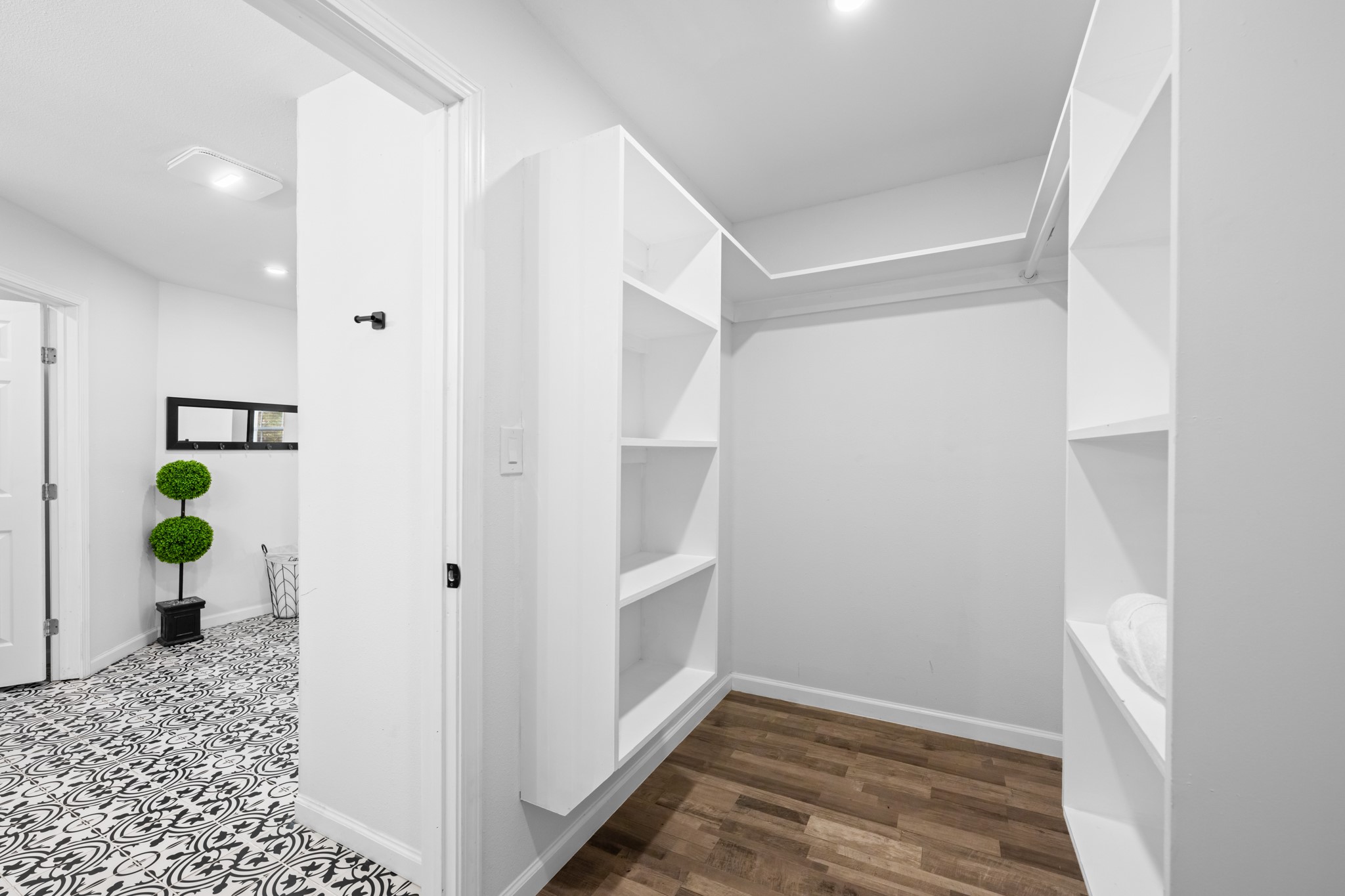 729 Kyle Angleton, TX 77515 - Photo 25 of 36 This photo showcases a spacious walk-in closet with white shelving and hanging space. It opens to a stylish area with patterned tile flooring and a decorative plant, providing a sleek and organized look.