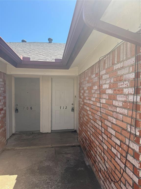 708 East Pecan Street, Unit 712 Hurst, TX 76053 - Photo 1 of 15 Brick exterior featuring two entry doors with secure deadbolts, a shingled roof, and an integrated gutter system