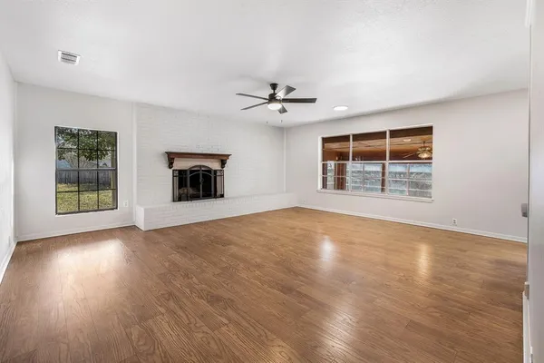 an empty room with wooden floor chandelier fan and windows