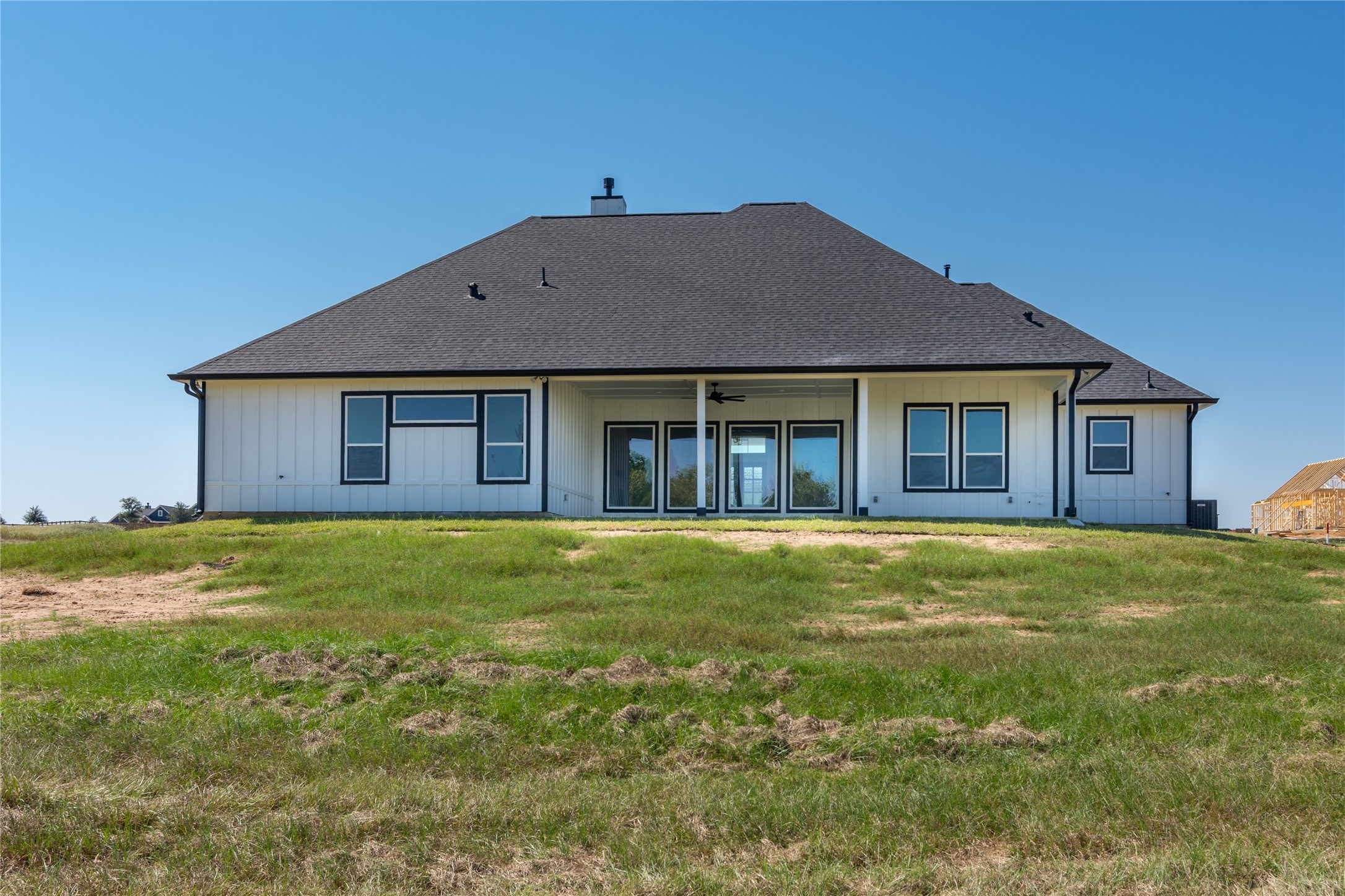 1404 Bluebonnet Ridge Drive Chappell Hill, TX 77426 - Photo 43 of 49 This photo showcases the back view of a modern single-story house with a large, sloped roof and a spacious patio area. The exterior features a crisp, white finish with contrasting dark window frames and a well-maintained lawn, providing an open landscape.