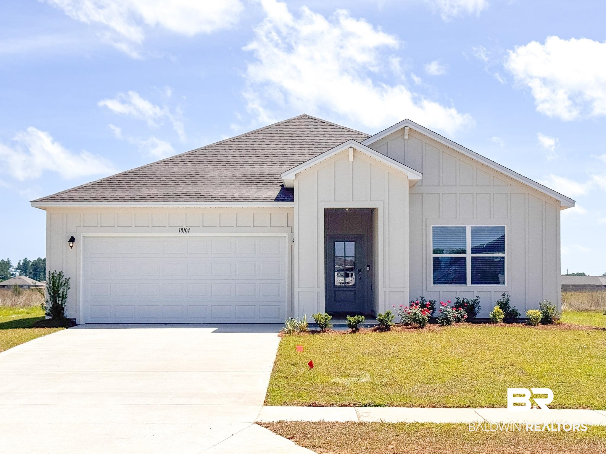 View of front of property with board and batten siding, a garage, a front yard, driveway, and roof with shingles