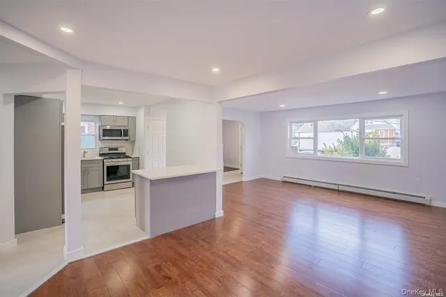 an empty room with wooden floor kitchen and windows