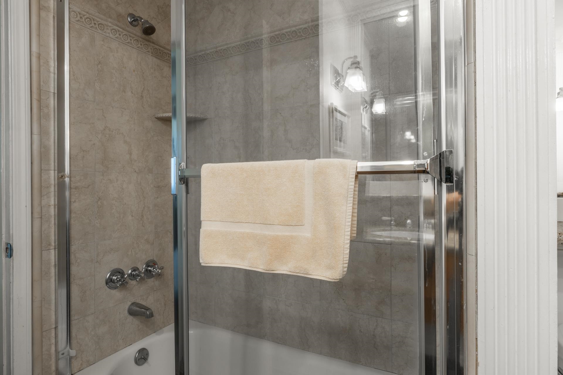 165 Old Mammoth Road, Unit 3 Mammoth Lakes, CA 93546 - Photo 21 of 48 Bathtub and shower combination featuring neutral-toned tile surround with decorative accent banding, chrome fixtures, and a clear glass shower enclosure