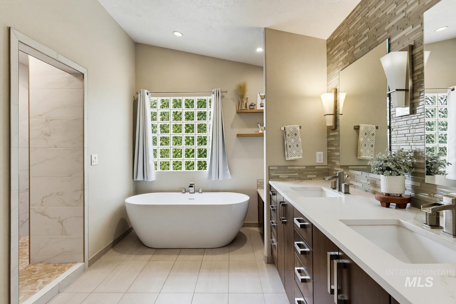 369 South Winthrop Way Boise, ID 83709 - Photo 29 of 50 Freestanding soaking tub with a glass block window, accompanied by a dual vanity featuring rectangular sinks and integrated storage
