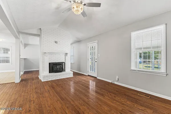 an empty room with wooden floor fireplace and windows