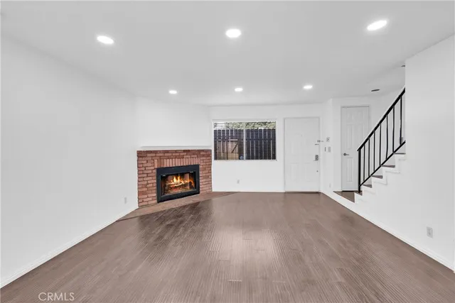 a view of an empty room with wooden floor fireplace and a window