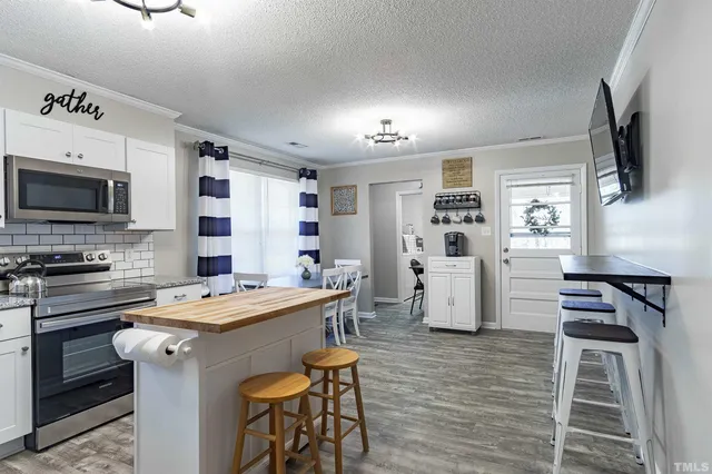 a open kitchen with stainless steel appliances granite countertop a stove top oven a refrigerator a dining table and chairs with wooden floor