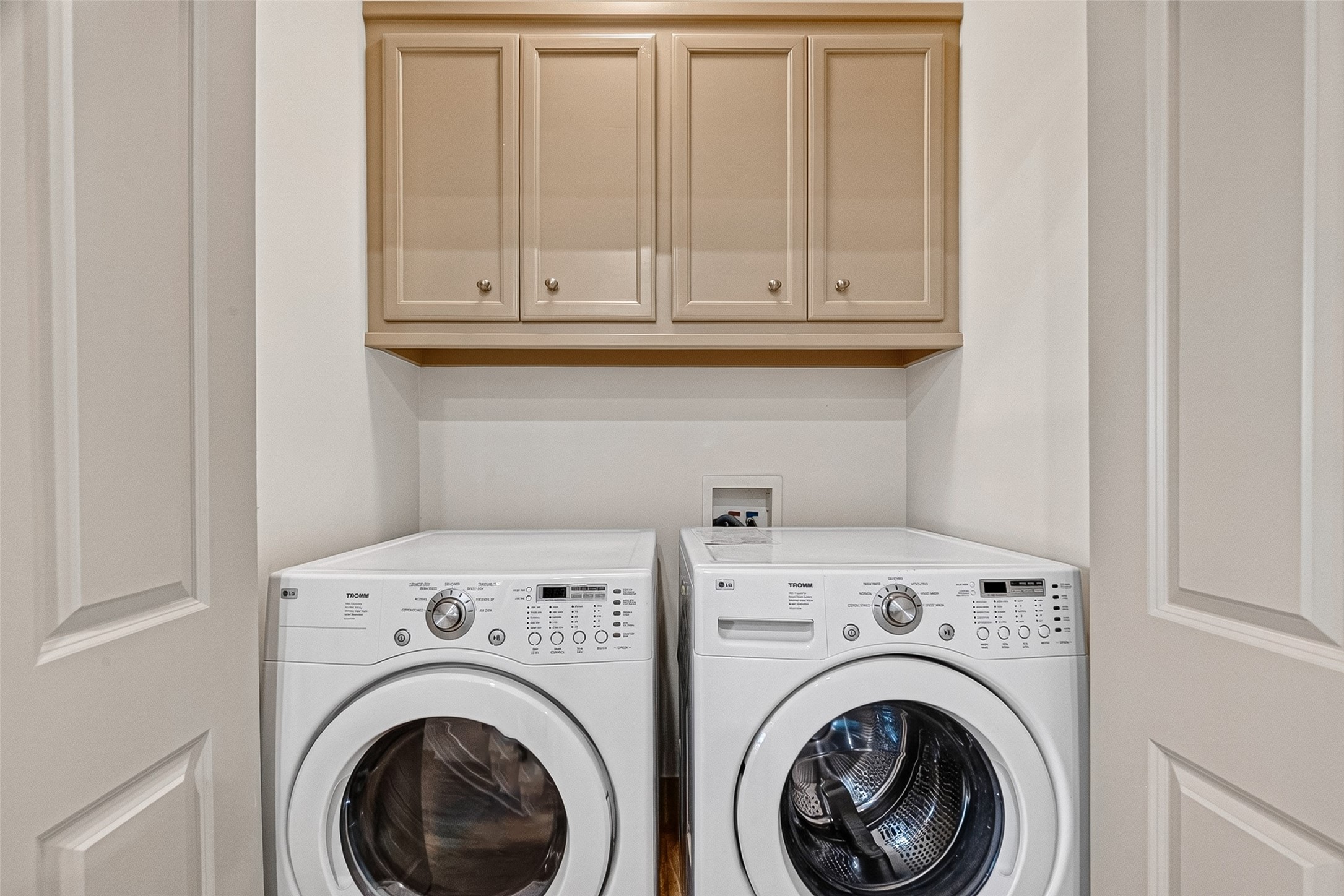2034 Colquitt Street, Unit A Houston, TX 77098 - Photo 24 of 41 This photo shows a compact laundry area with a front-loading washer and dryer set. Above them are beige cabinets for storage, providing a clean and efficient space for laundry needs. Washer & Dryer included!